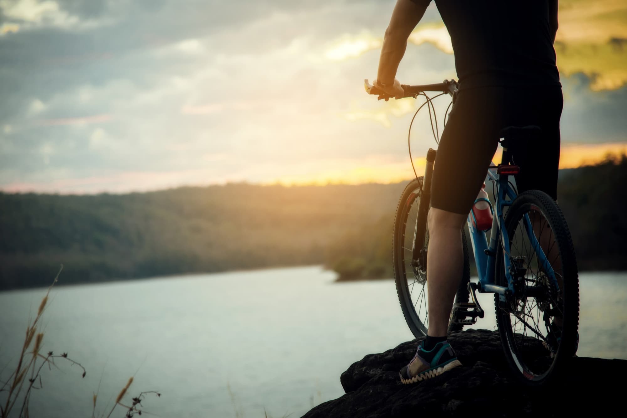 Cyclist silhouetted at lakeside during golden hour sunset ride