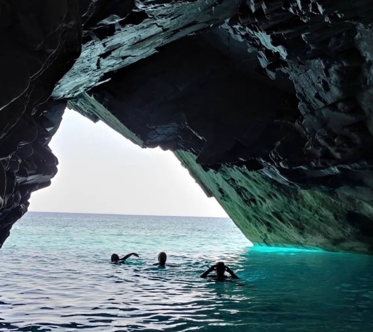 Swimmers exploring turquoise sea cave entrance off Skiathos