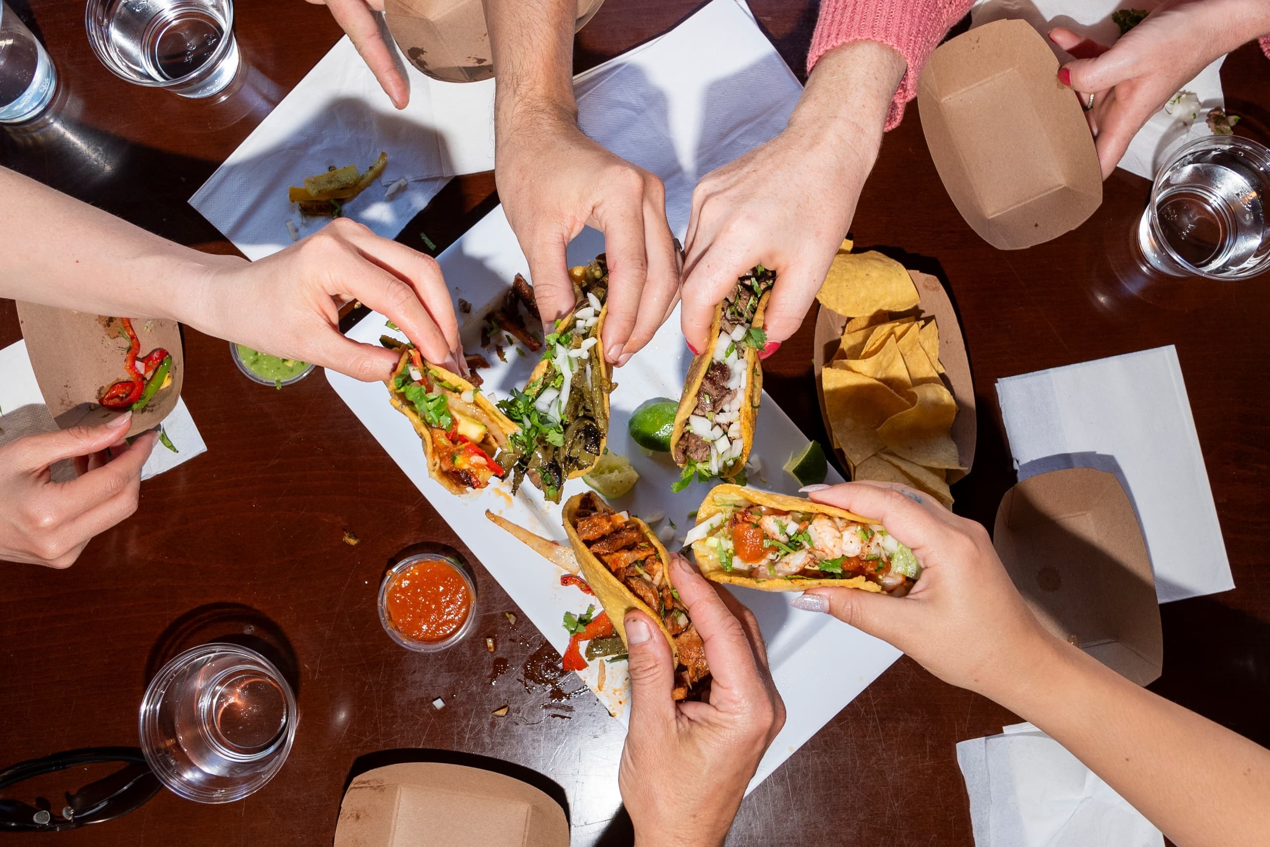 Friends sharing tacos and drinks over communal table