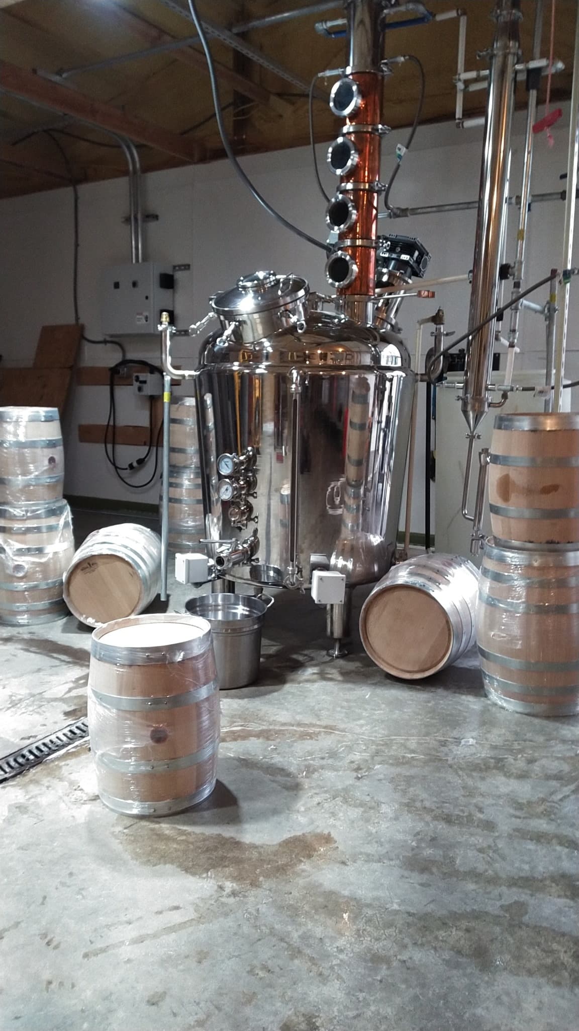 Stainless distillation still and oak barrels inside craft distillery