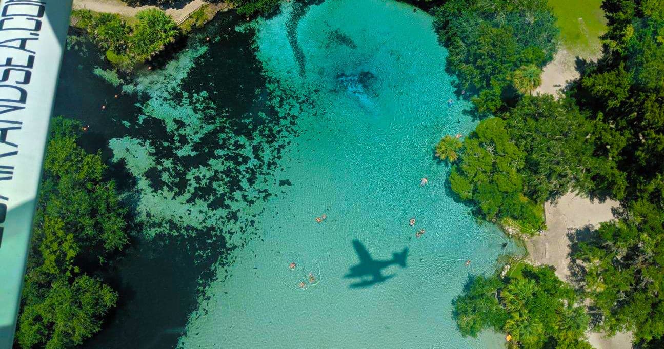 Aerial turquoise spring with seaplane shadow over clear water