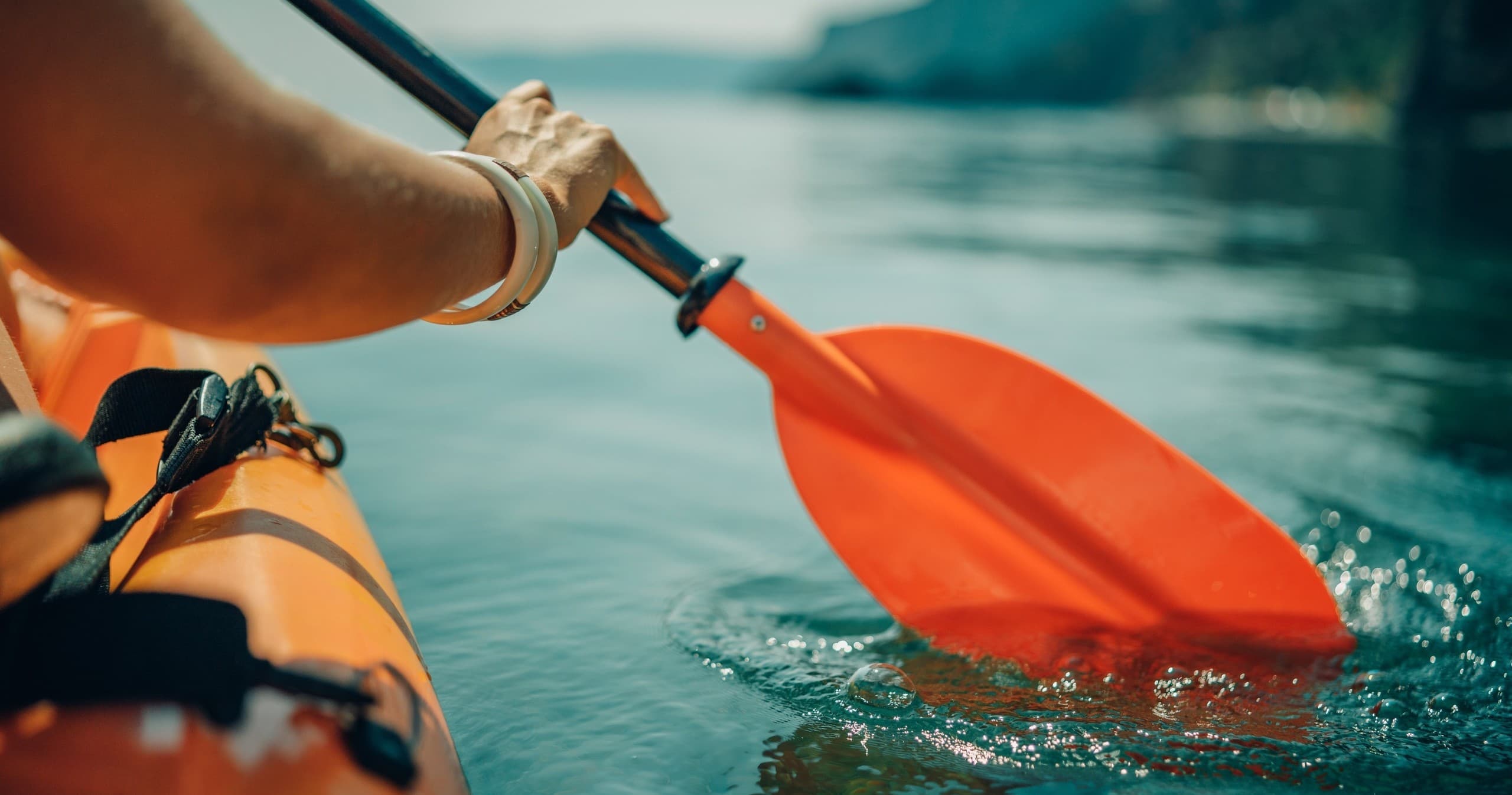 Close-up kayak paddle dipping into clear coastal water, action
