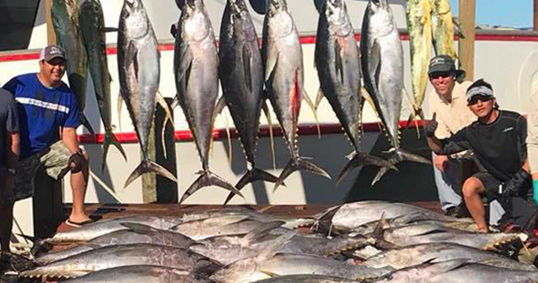 Charter fishing crew with large tuna catch hung on boat rail