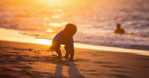 Child playing on beach at golden sunset, shoreline silhouette