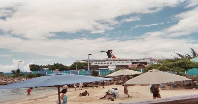 Beachgoers on sandy beach with cruise ship docked offshore