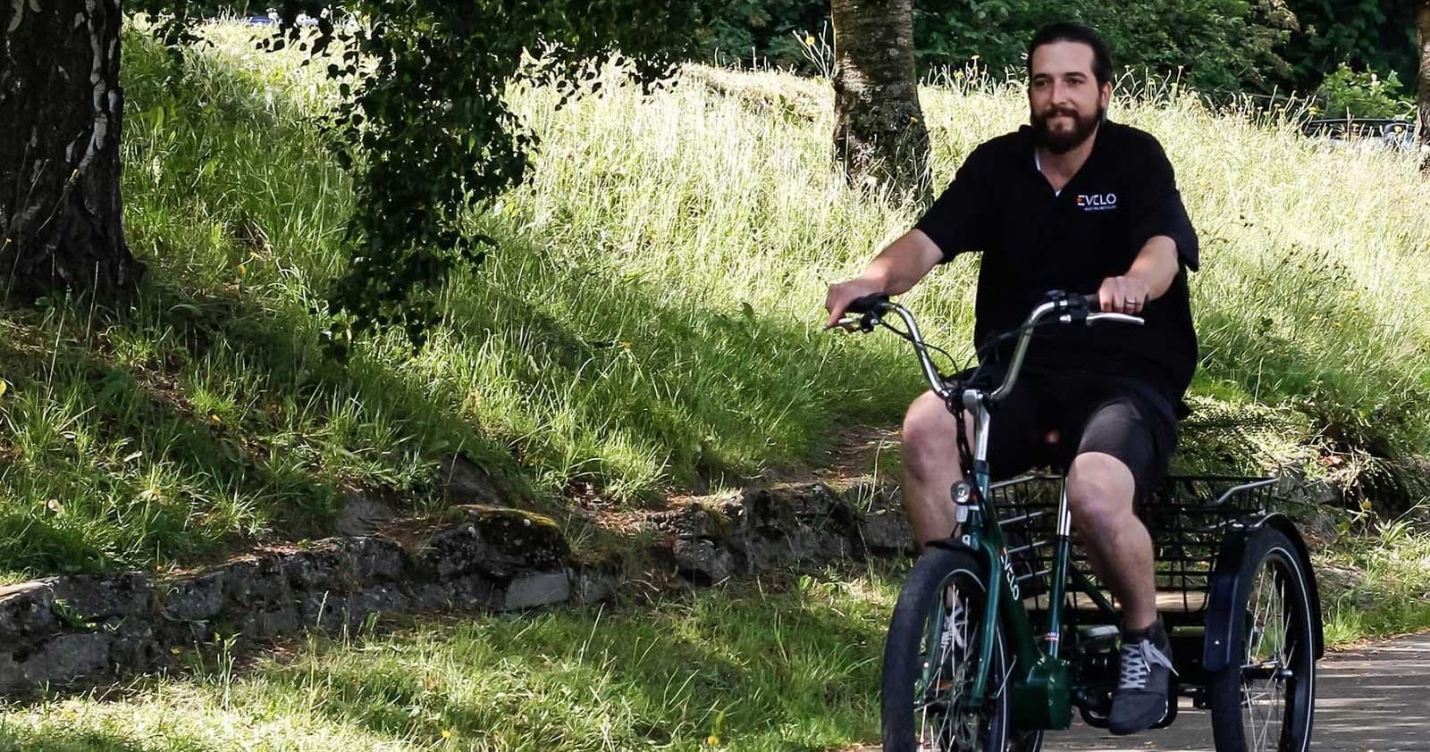 Man riding adaptive trike through grassy park trail on sunny day