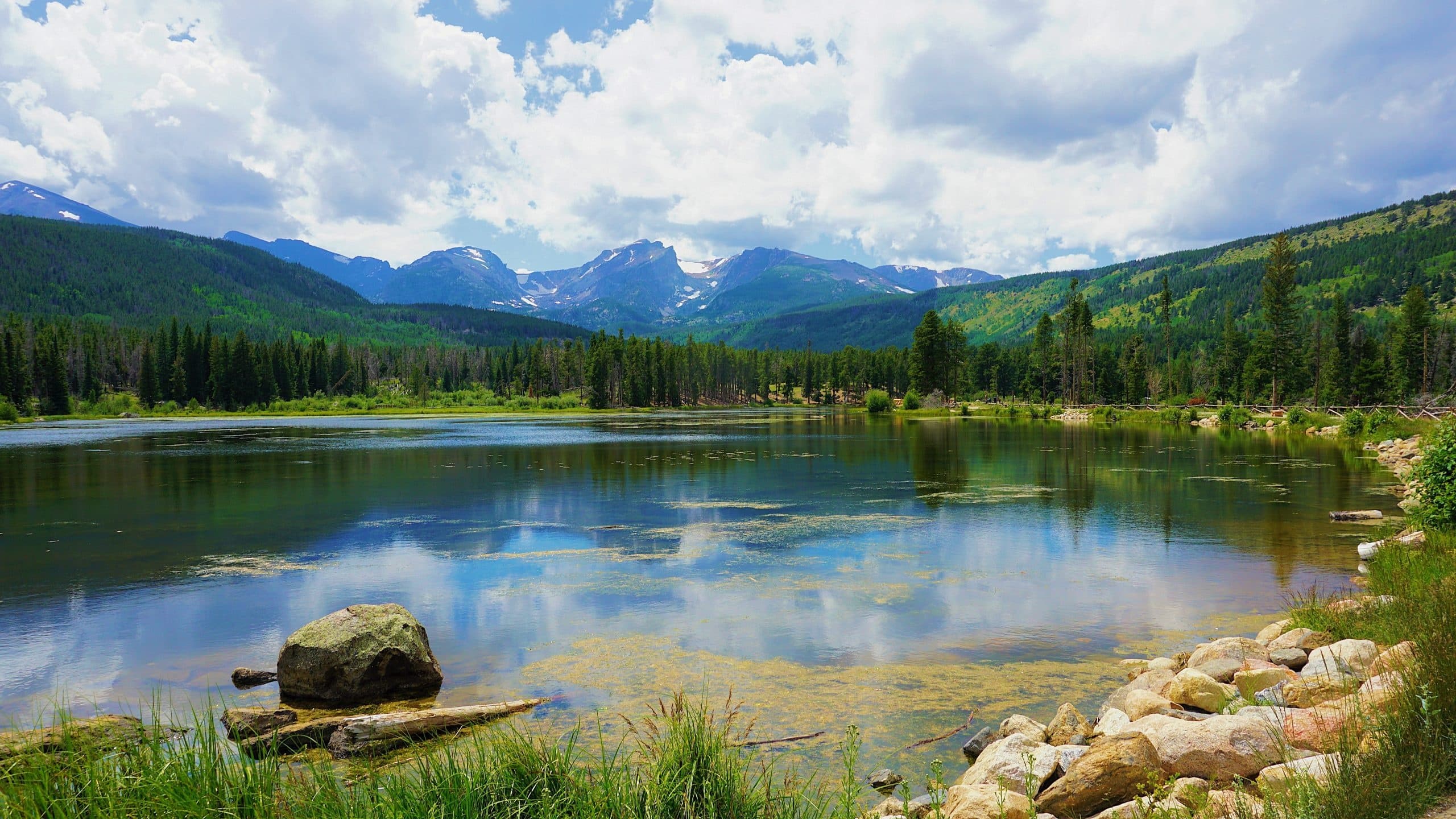 Clear alpine lake reflecting mountain peaks and evergreen forest