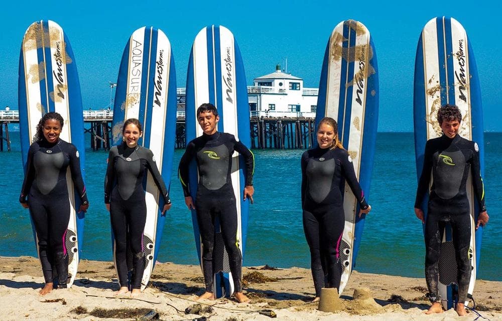 Surfers standing with boards on a sunny sandy beach by pier