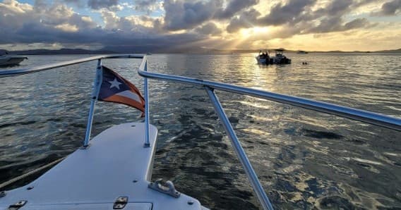 Boat bow cruising at sunset with flag, coastal marine scenery