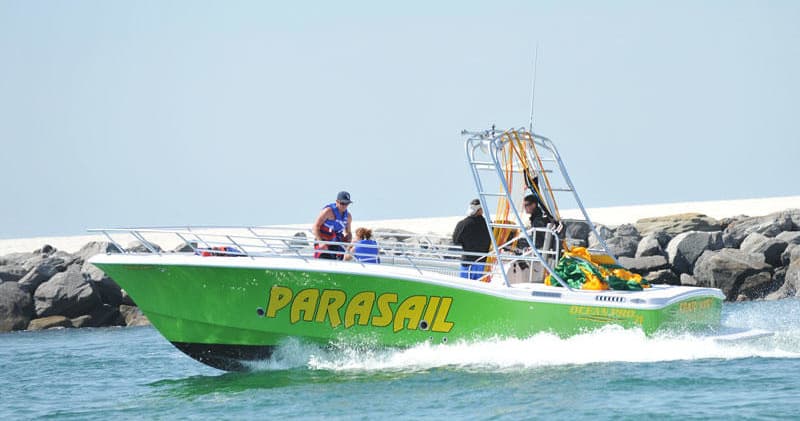 Speedboat towing parasail off rocky shoreline with blue sea