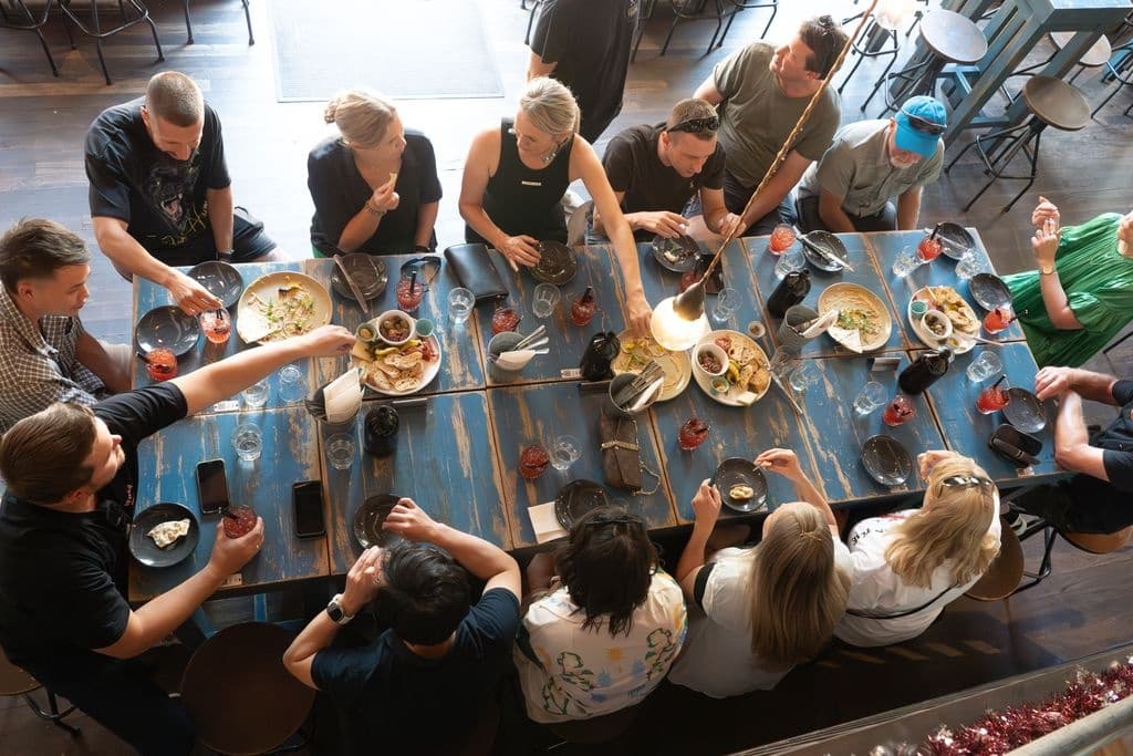 Group dining at long communal table inside urban restaurant