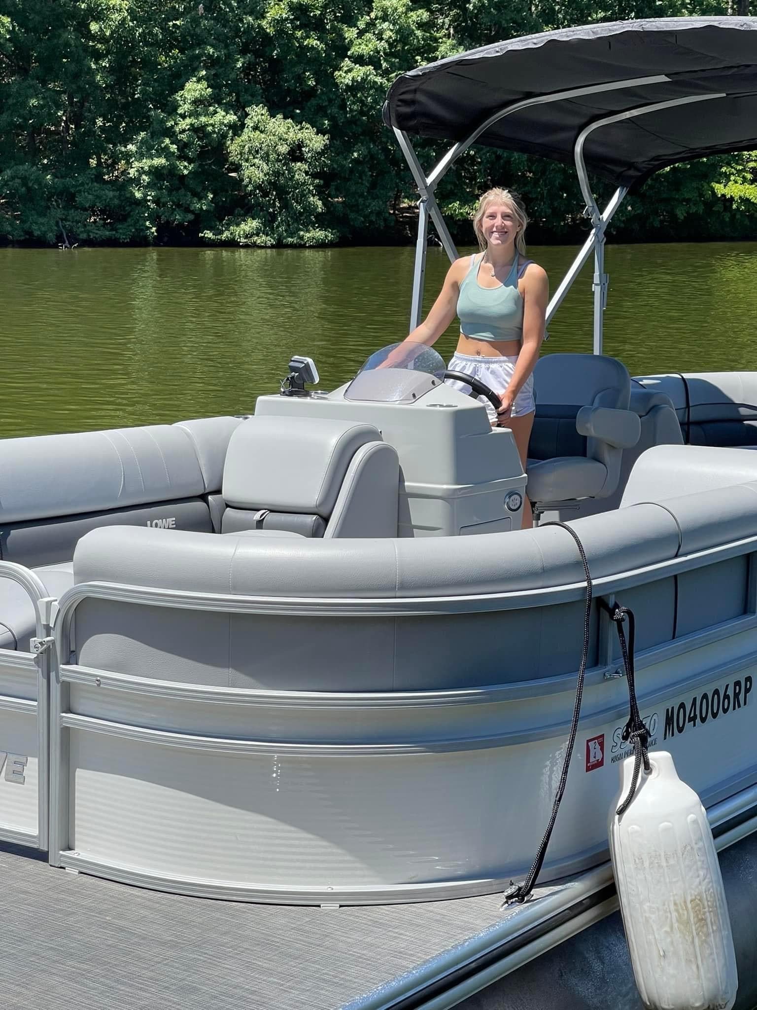 Woman standing at helm on docked pontoon with lake background