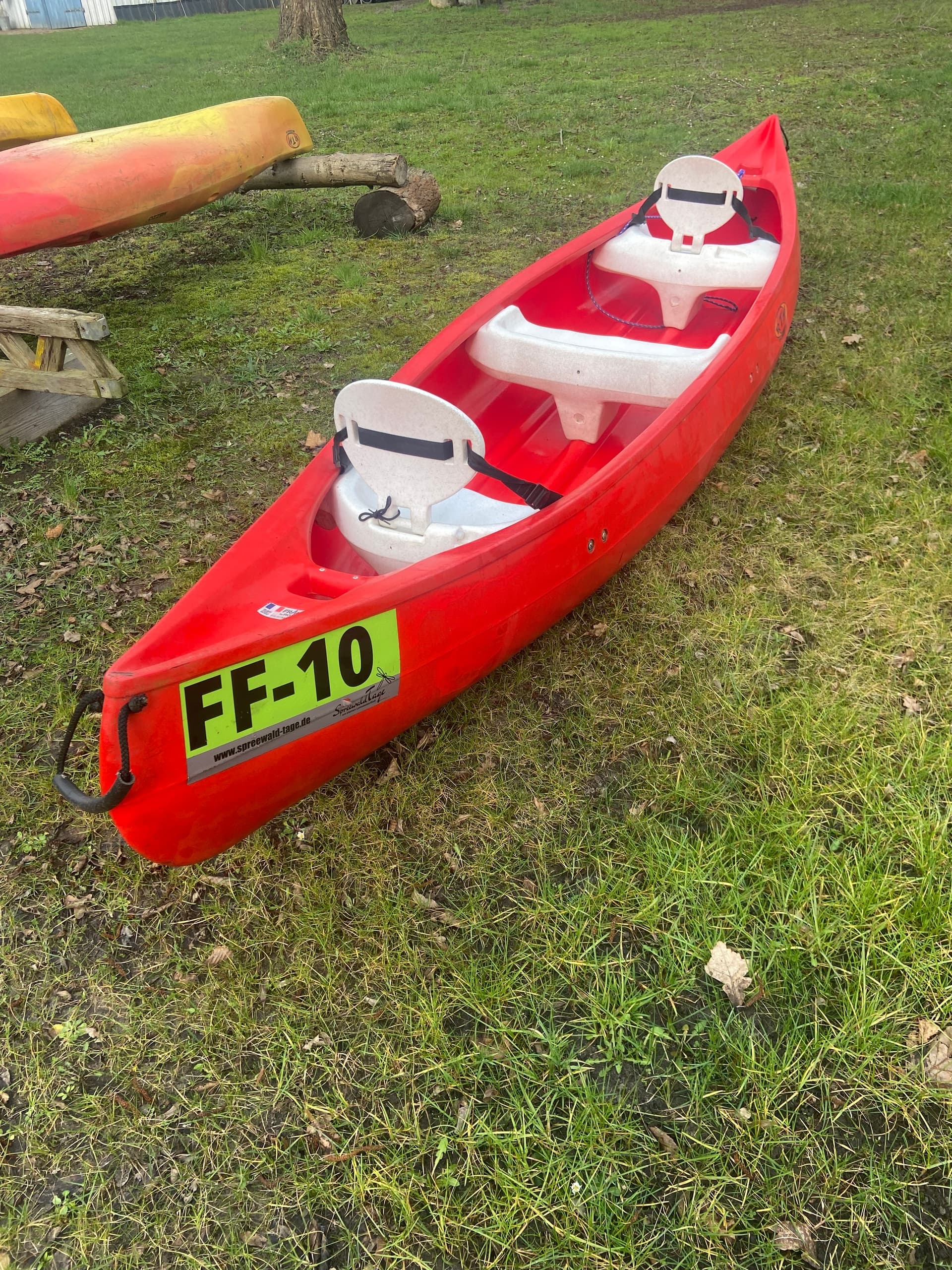 Red tandem canoe resting on grassy park lawn, numbered FF-10