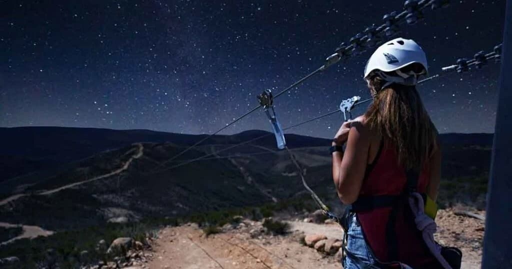 Woman preparing to zipline over desert mountain under starry sky