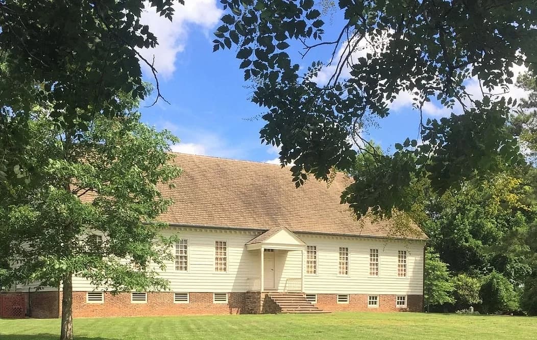 White historic meetinghouse framed by trees on grassy lawn