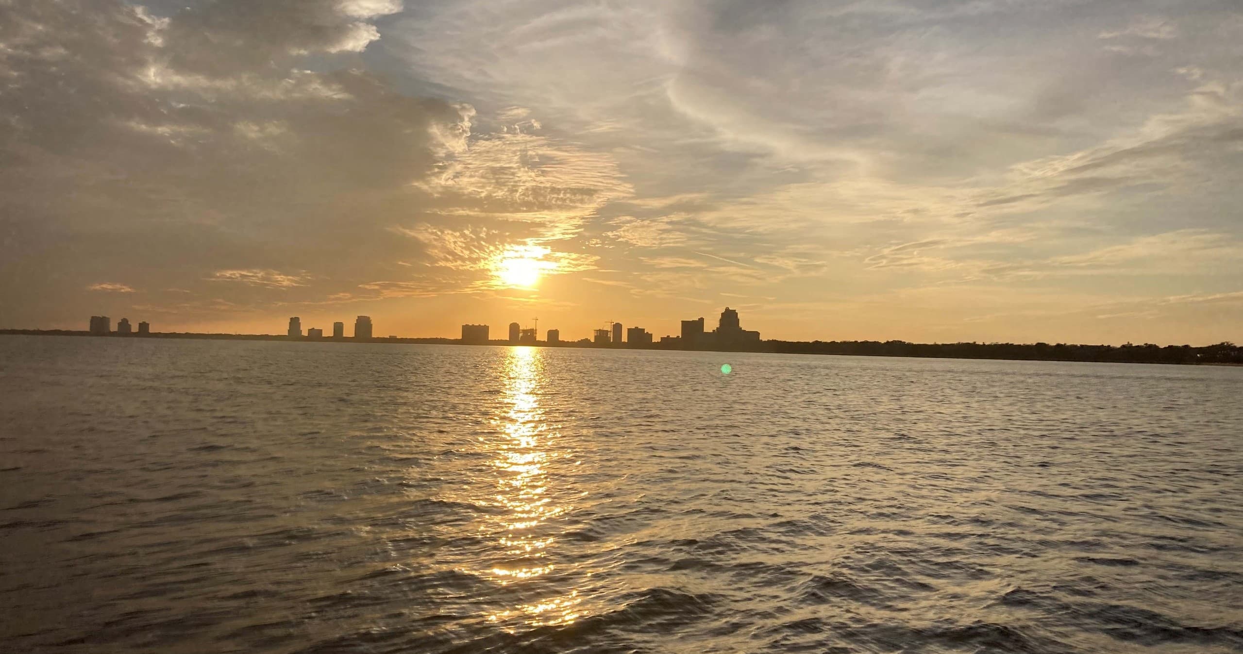Sunset boat cruise across bay with city skyline on horizon