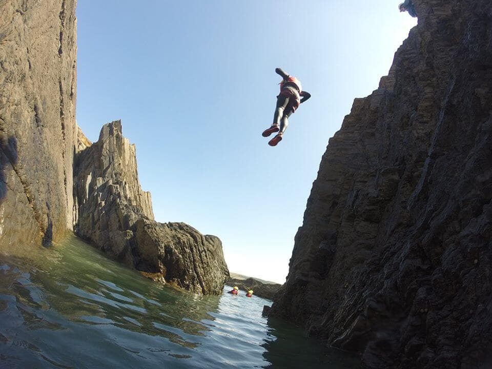 Cliff jumper leaping into tidal sea between rugged rock walls