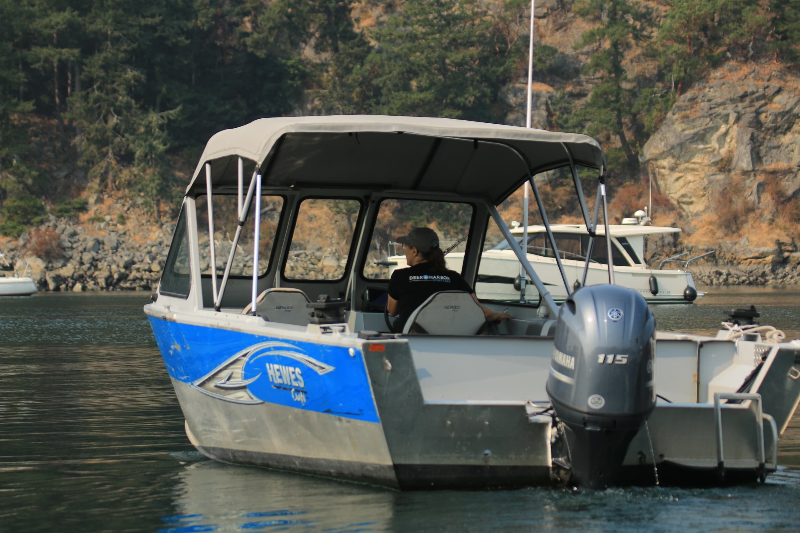 Blue aluminum skiff with outboard engine cruising near rocky forested shoreline