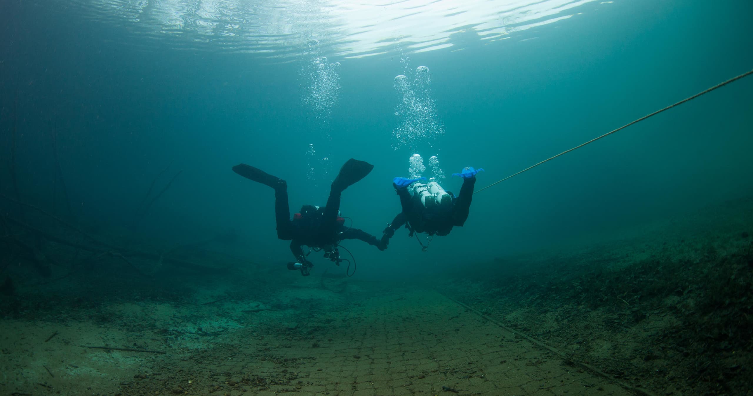 Scuba divers descending along guideline in open lake water