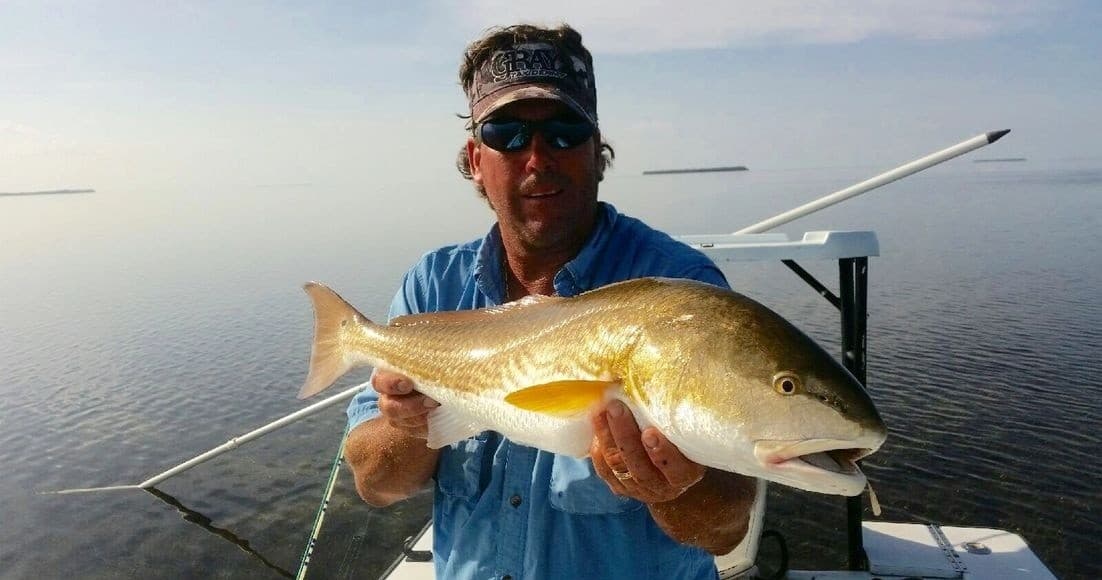 Angler holding redfish on flats with calm ocean horizon