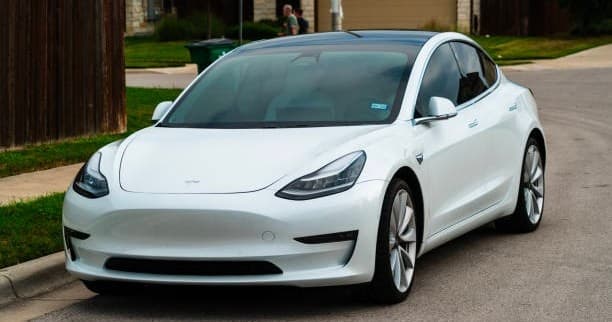 White electric car parked on suburban street by houses