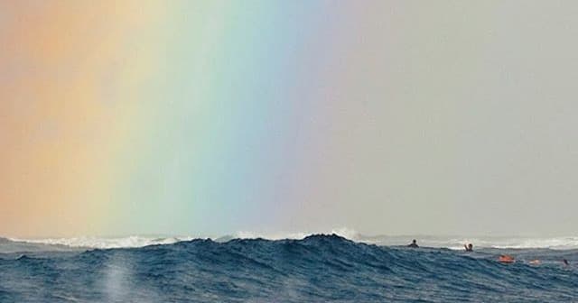 Ocean waves with rainbow and surfers in scenic coastal surf