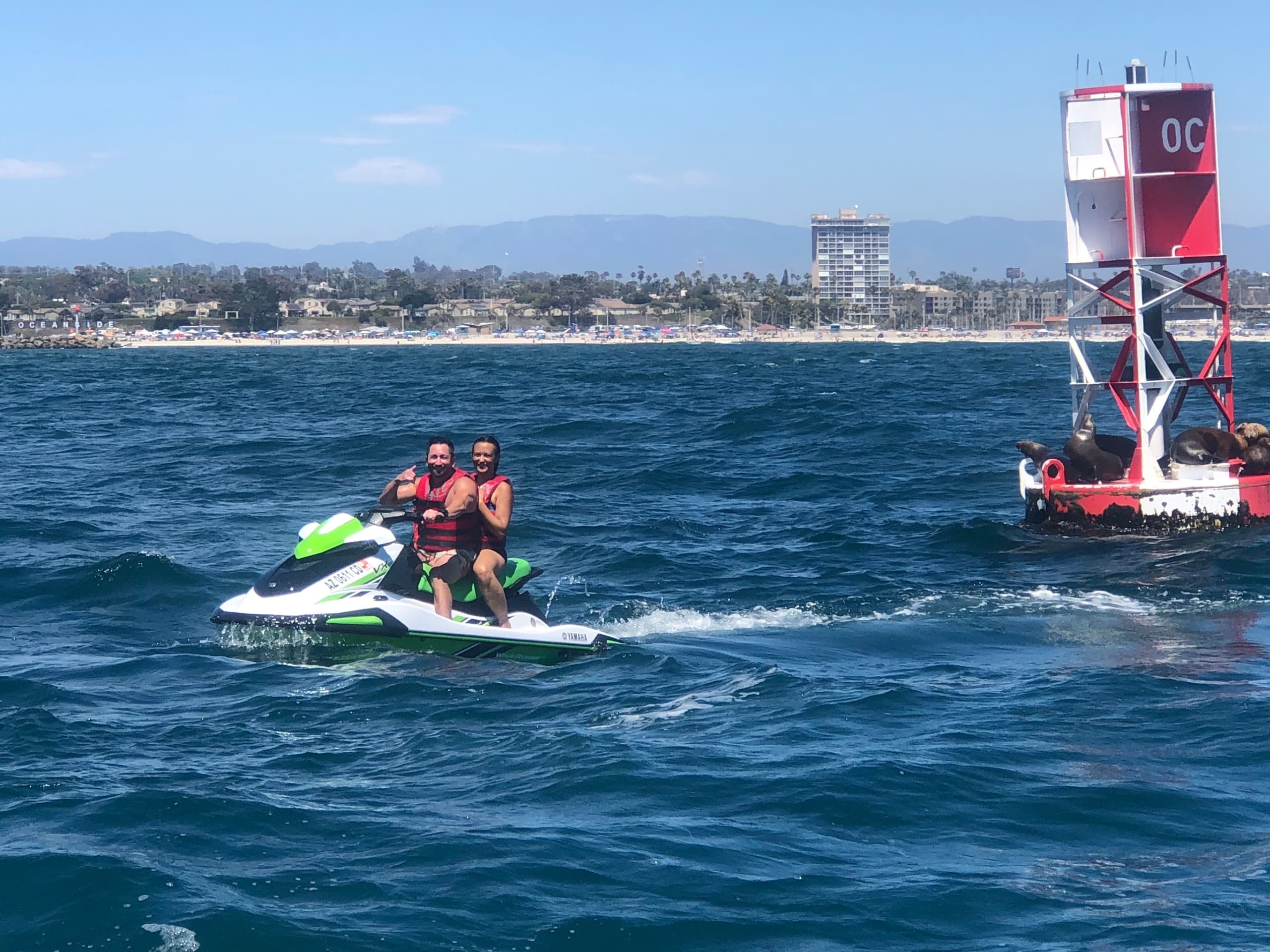 Two riders on jetski navigating open ocean near coastal buoy