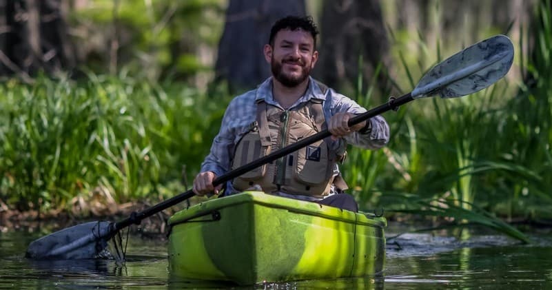 Kayaker paddling a green kayak through marshes in Louisiana