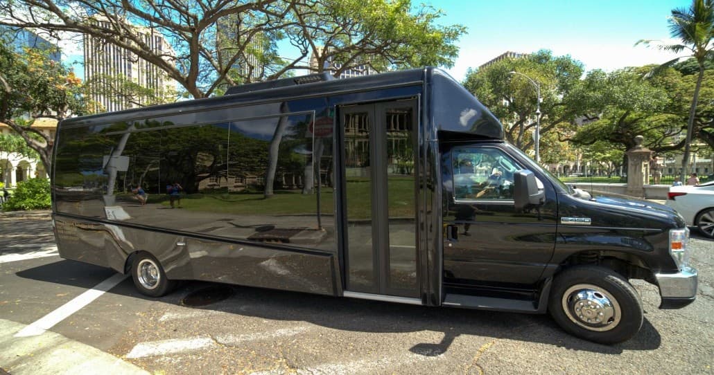 Large black shuttle with open door parked on leafy city block
