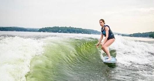 Wake surf rider riding boat wake on forested lake shore