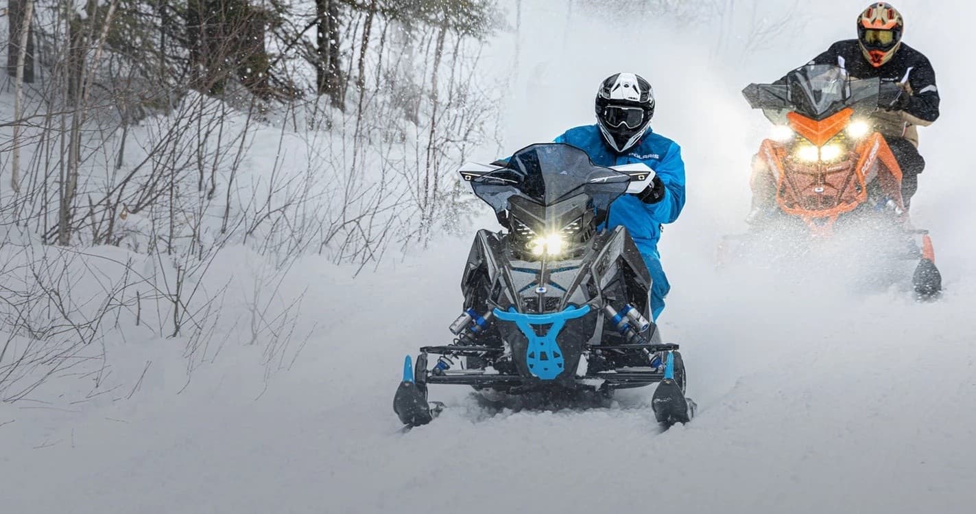 Snowmobilers racing through snowy forest trail at speed