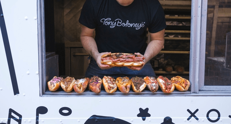 Person serving artisan subs from outdoor food truck window at market