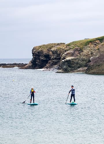 Two paddleboarders touring calm coastal bay near rocky headland