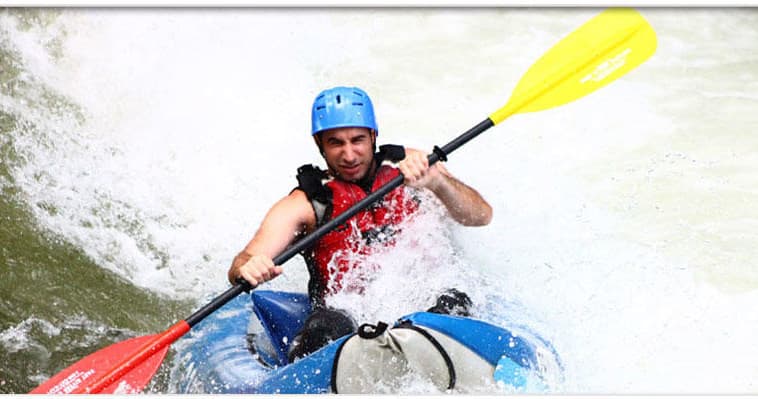 Solo kayaker navigating steep whitewater wave on scenic mountain river