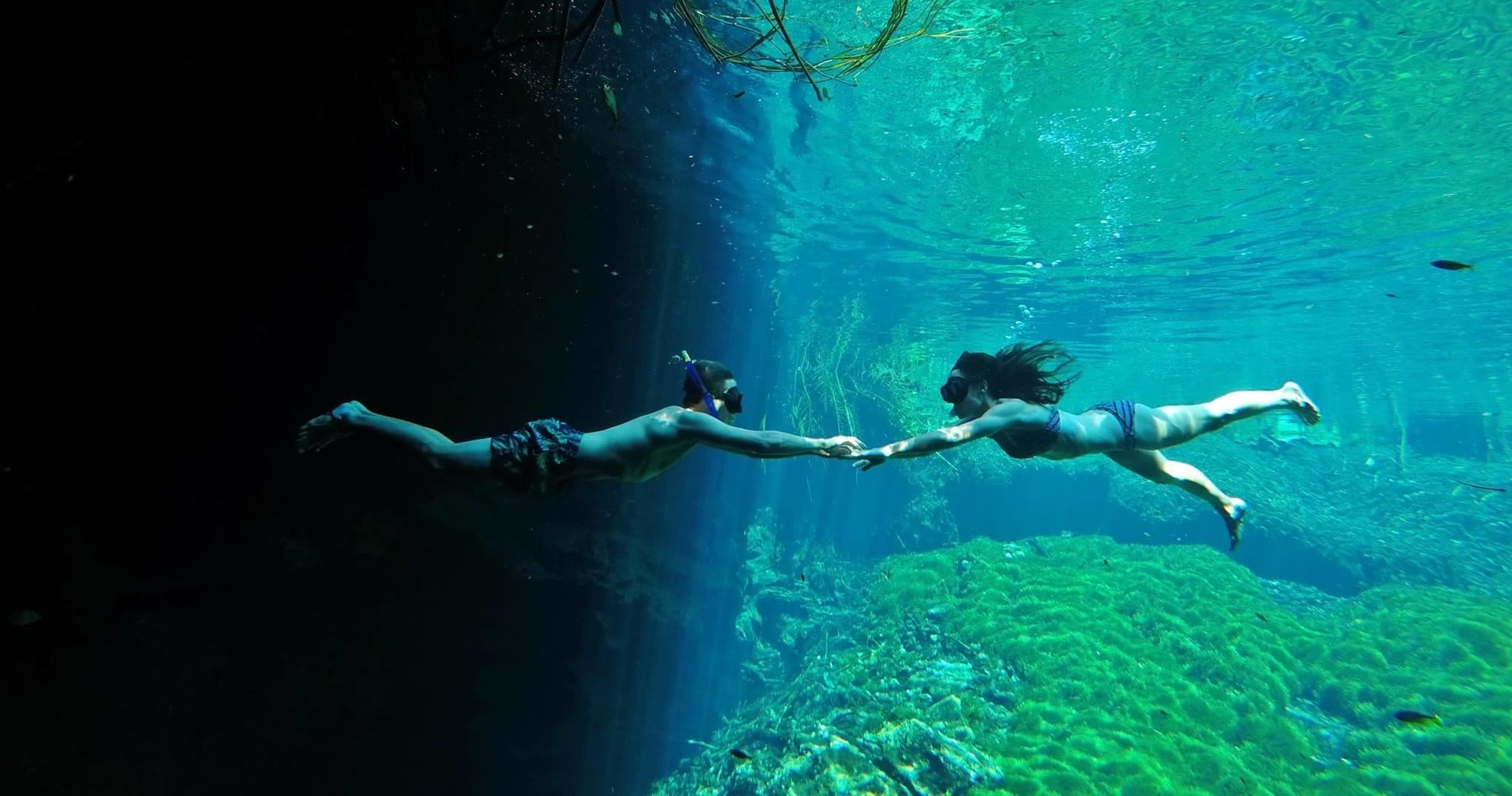Snorkelers swimming through clear cenote passage, underwater cave