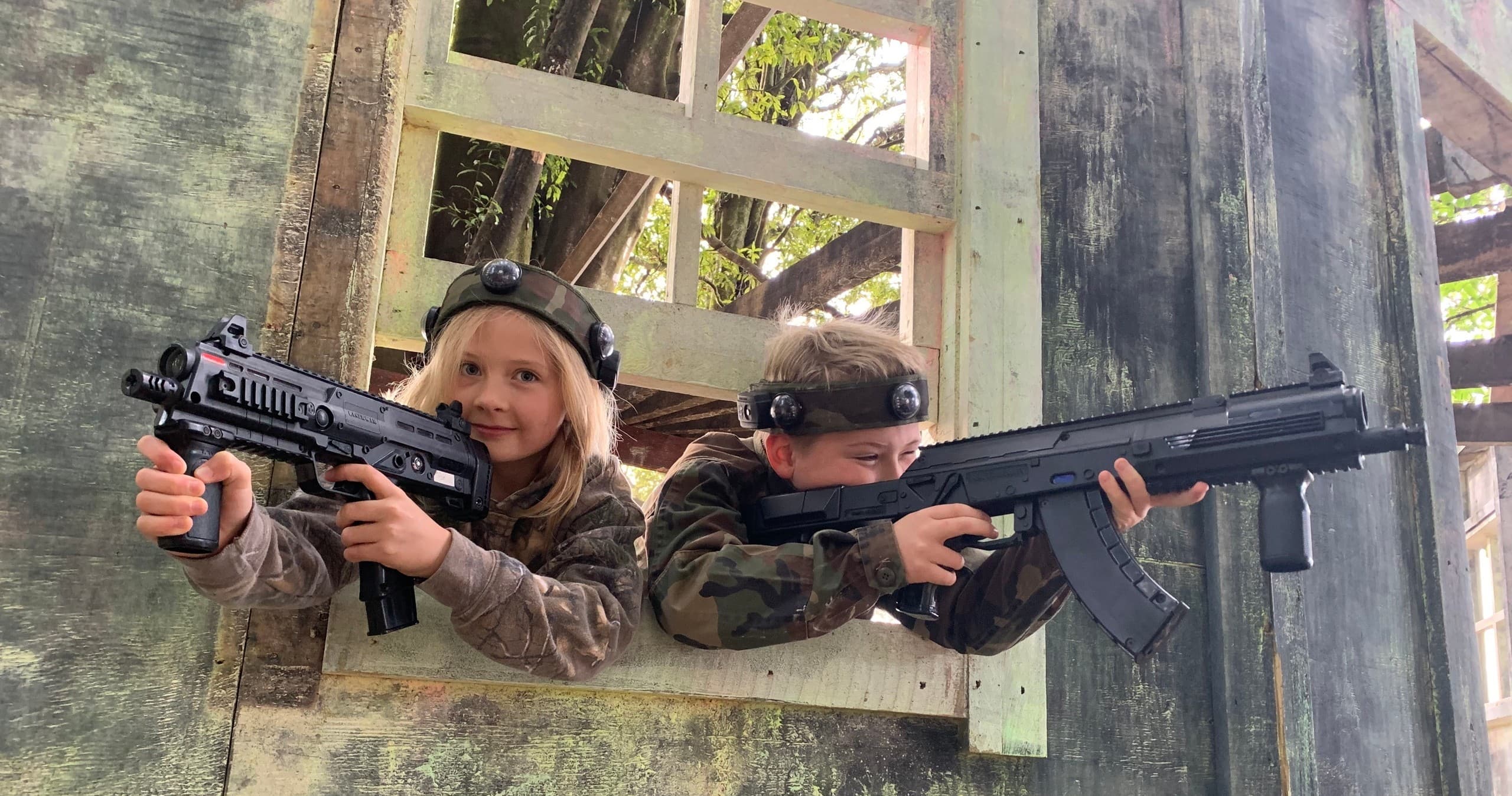 Kids aiming replica rifles from wooden fort in forest game