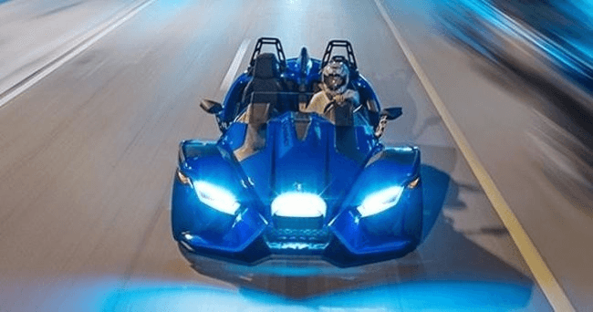 Blue Slingshot speeding at night on illuminated coastal road