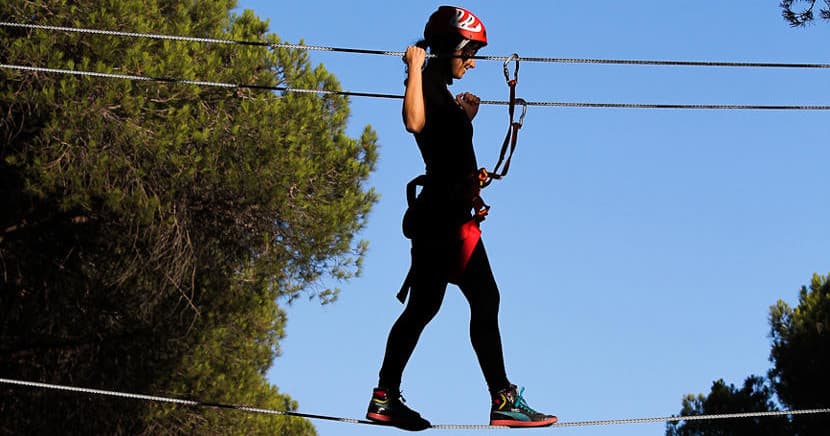 Person tightrope walking high between trees against blue sky