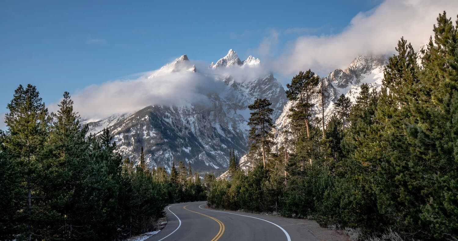 Scenic mountain highway approaching Grand Teton Range at dawn