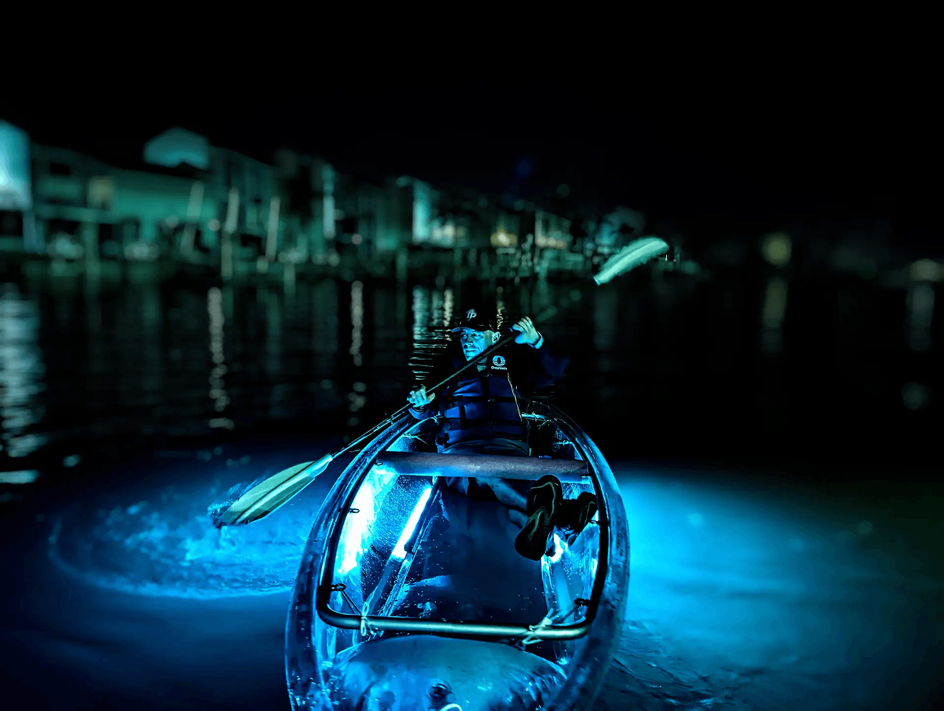 Paddler in illuminated clear kayak on coastal waters at night