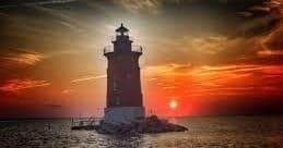 Historic lighthouse silhouetted against vibrant ocean sunset