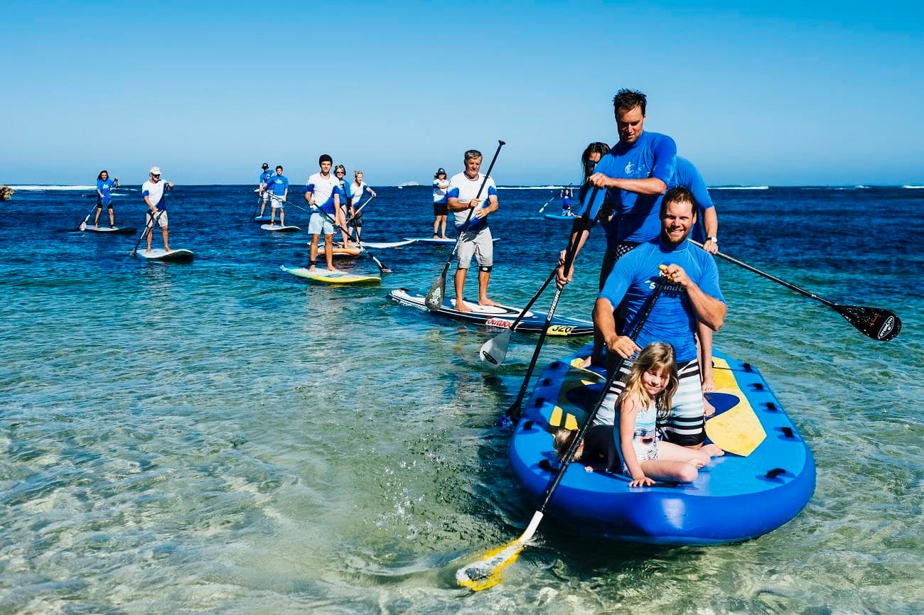 Group paddleboarding and inflatable kayak launching in coastal shallows