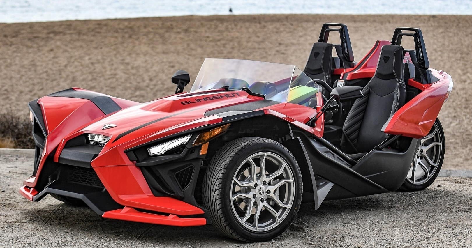 Red Slingshot three-wheeled roadster parked by ocean beach, scenic drive