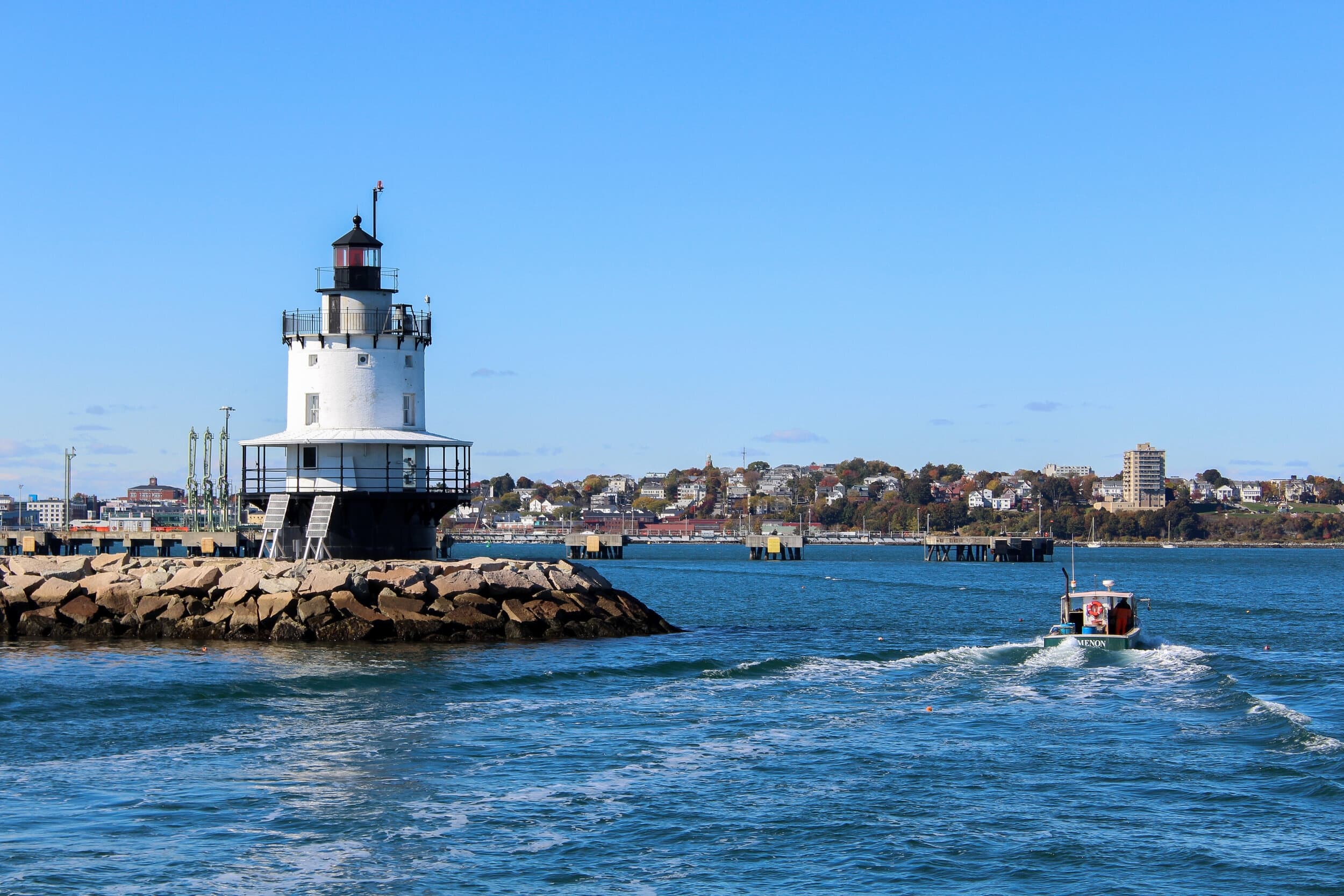 Small harbor lighthouse with boat approaching, coastal boat tour