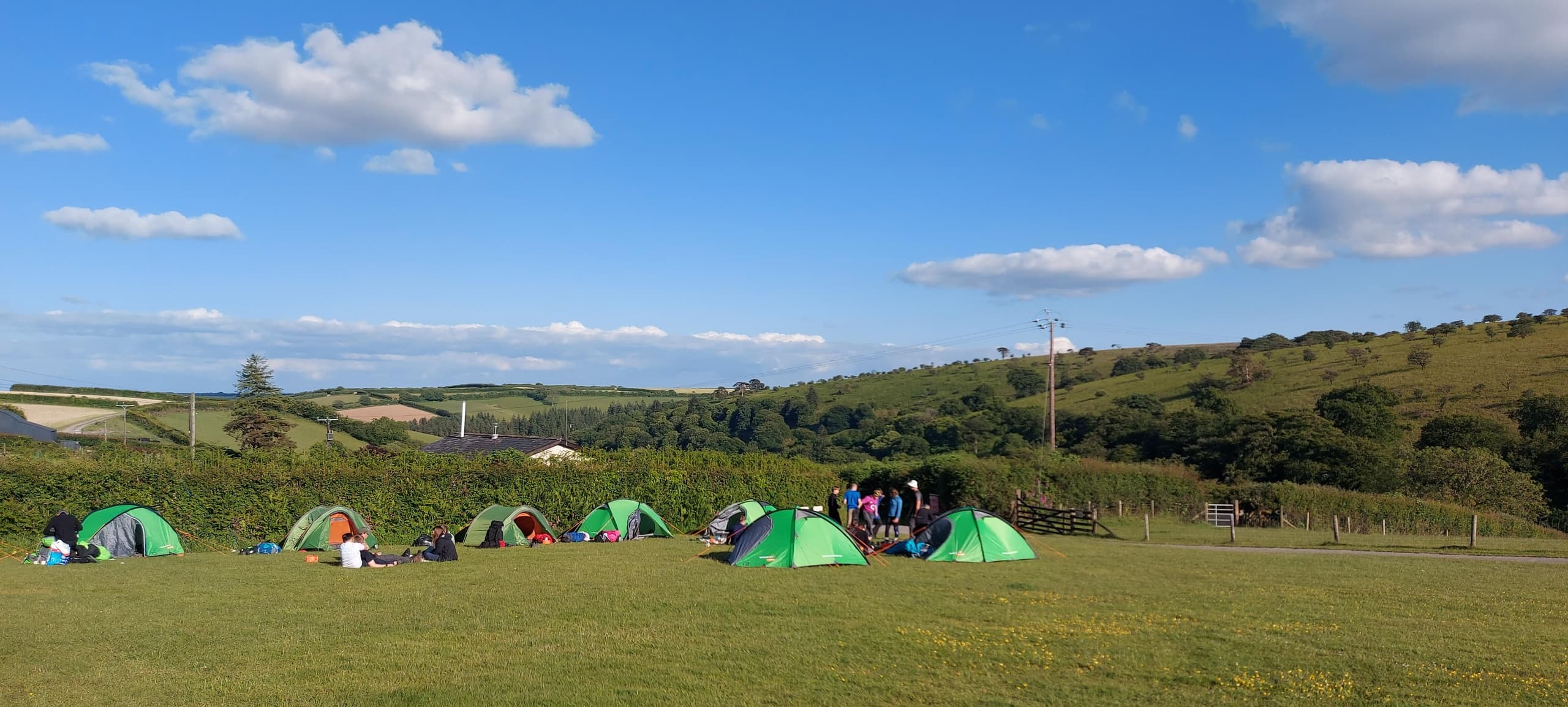 Green tents pitched on open hillside campsite under blue sky