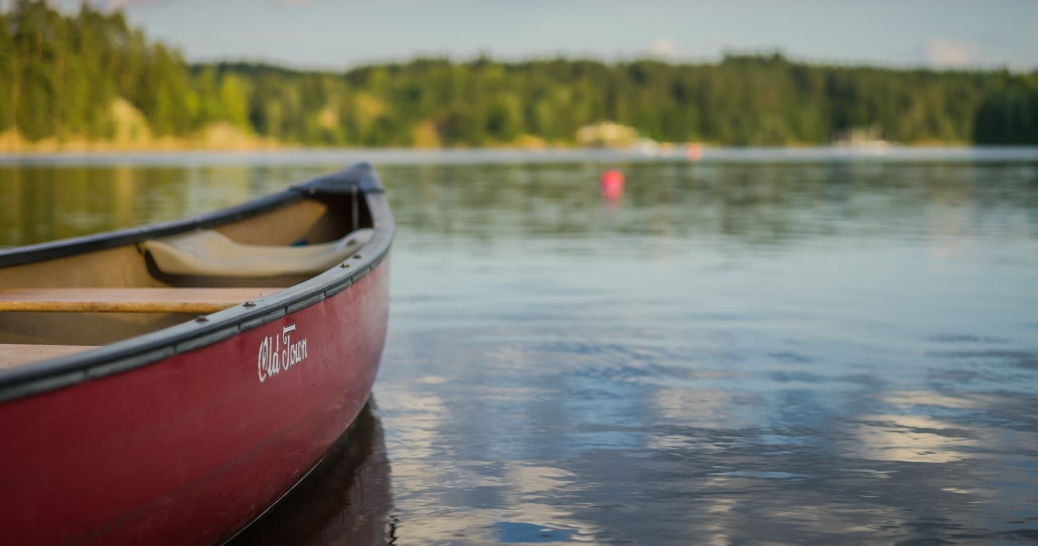 Red canoe gliding on calm forest lake at sunrise