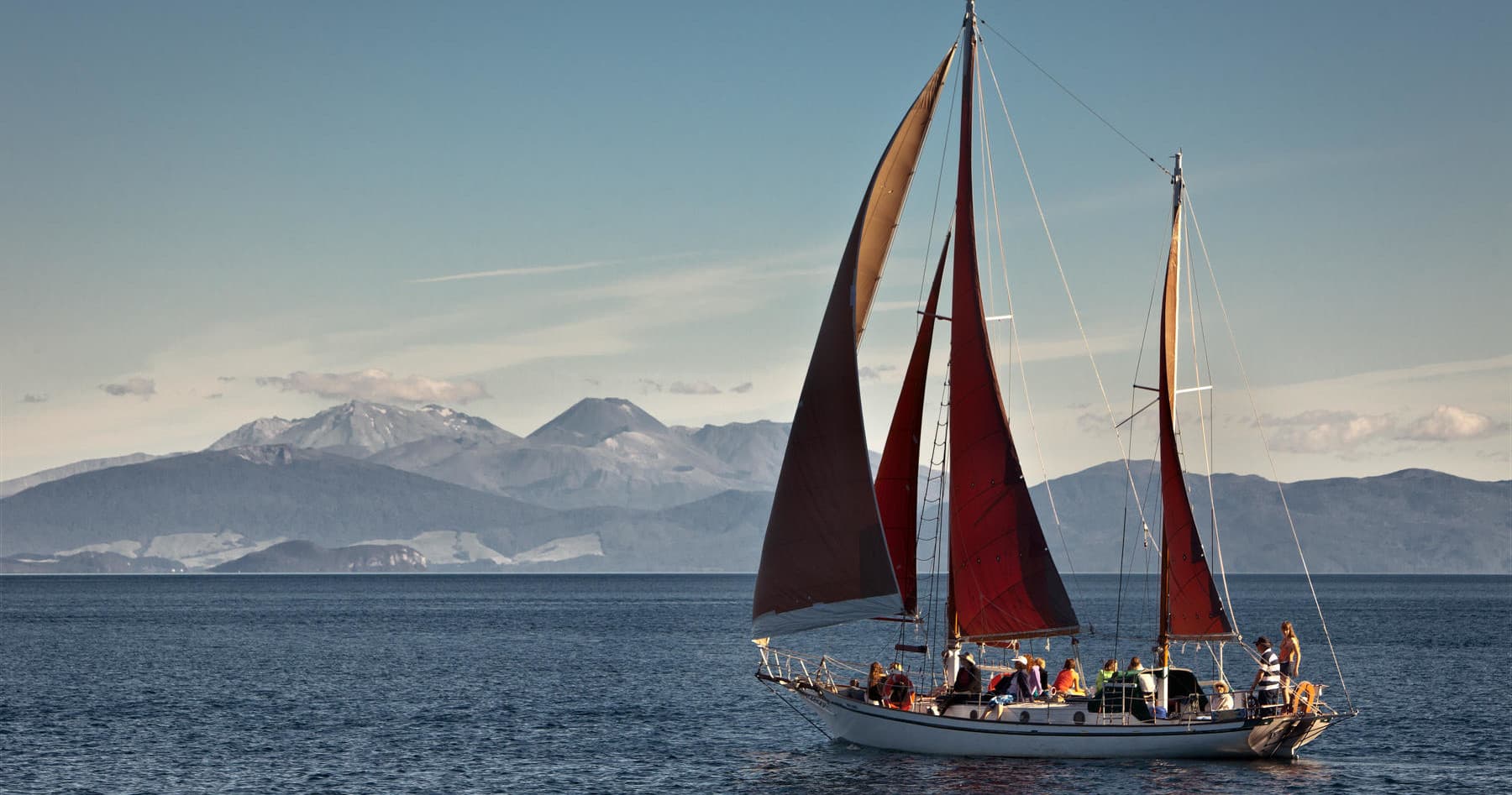 Classic sailboat with red sails cruising past mountain coast