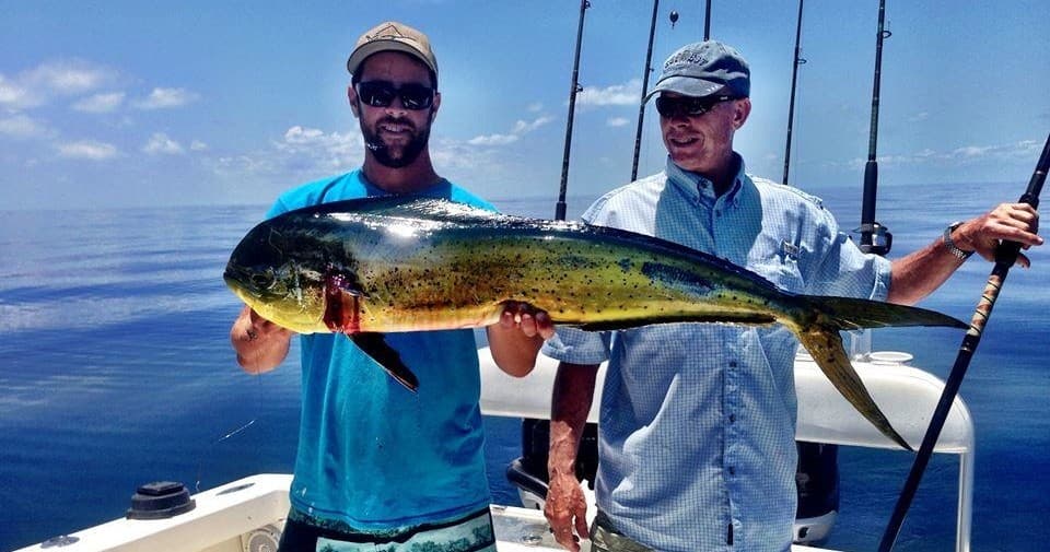Anglers holding a mahi-mahi on a sportfishing boat in open ocean