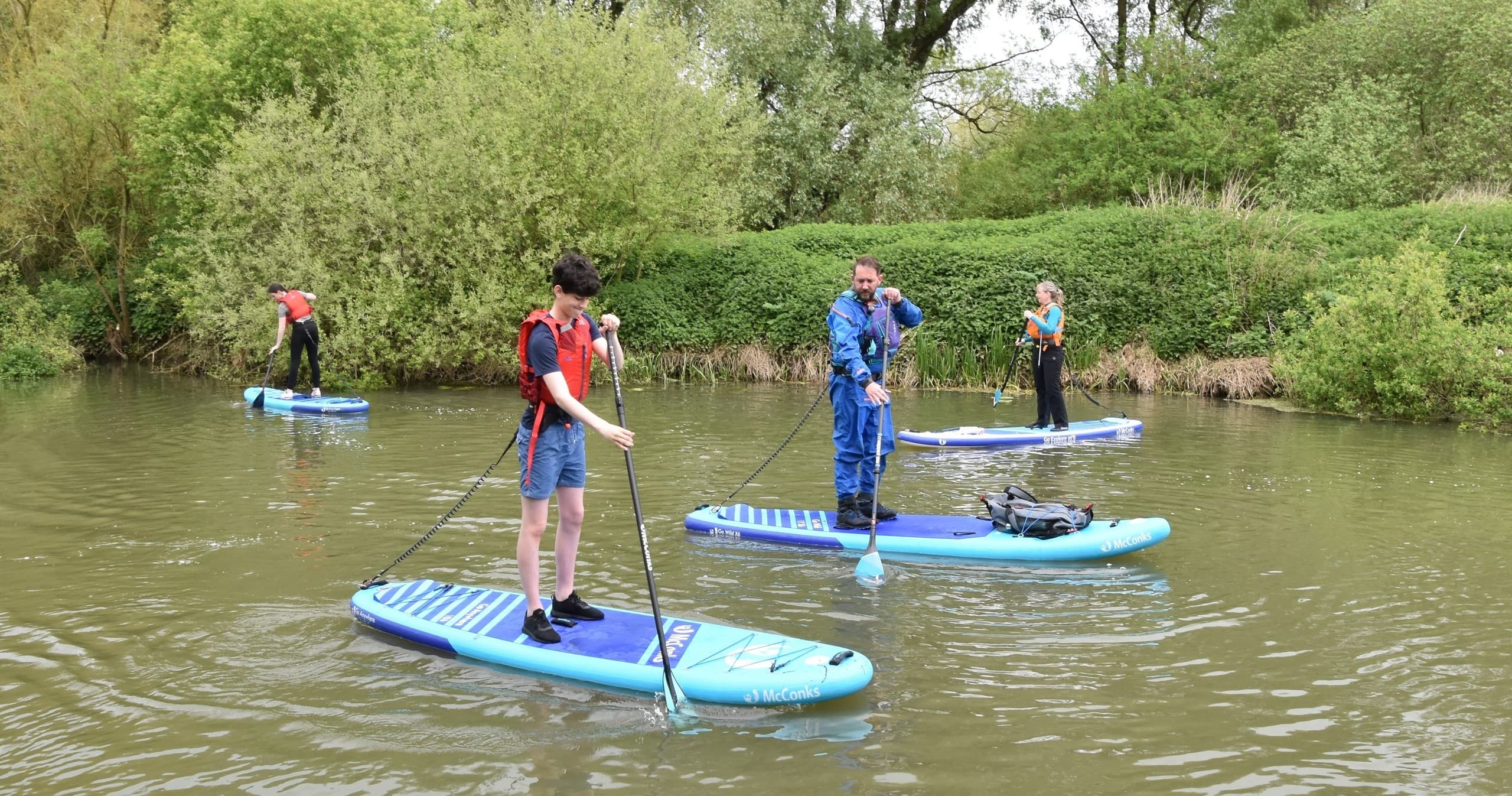 Beginners stand-up paddleboarding on a green river bend