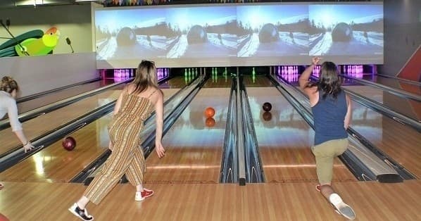 People bowling at indoor alley with multiple lanes and screens
